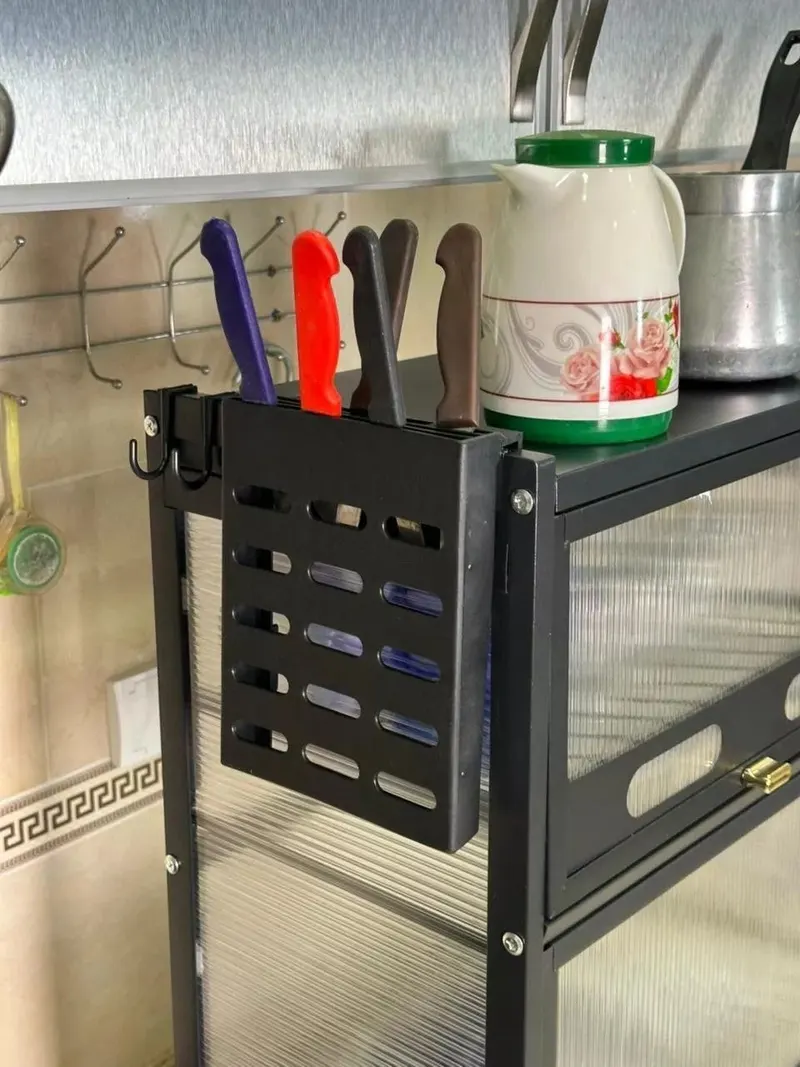 حمّالة كحلة فيها ثقوب معلقة على جنب الخزانة وفيها جناوي، وحداها جوج خطاطف صغار